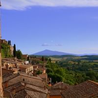 Vue de Montepulciano montrant des toits en terre cuite, des cyprès et des collines toscanes avec une montagne lointaine sous un ciel bleu.