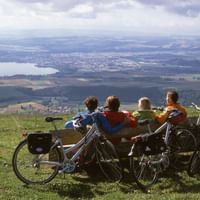 Quatre cyclistes assis sur un banc en bois surplombant le paysage du Jura suisse près de Sainte-Croix, vélos garés à proximité.