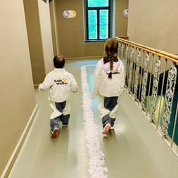 Deux enfants portant des vestes de protection blanches Salzwelten marchent dans un couloir de musée avec des balustrades ornées et une fenêtre.