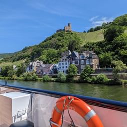 Vue de Bernkastel-Kues depuis le pont d'un bateau montrant des bâtiments historiques le long de la Moselle avec ruines de château sur colline viticole.