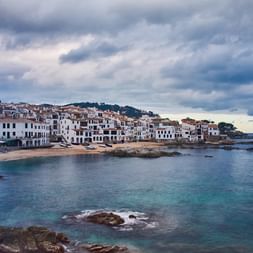Calella de Palafrugell sur la Costa Brava avec bâtiments blancs le long des eaux turquoise de la Méditerranée, côte rocheuse et ciel nuageux.