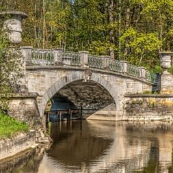 Pont Visconti en pierre avec une arche et des urnes décoratives enjambant une eau calme, entouré d'arbres verts luxuriants.