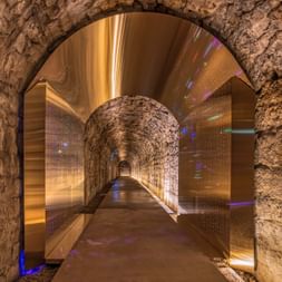 Tunnel en pierre illuminé dans les Casemates de la Pétrusse, Luxembourg, avec plafond voûté et éclairage moderne créant des reflets colorés.