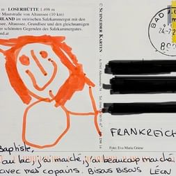 Carte postale de Léon avec dessin au crayon orange d'un personnage souriant, timbre autrichien et texte français manuscrit sur la randonnée au Salzkammergut.