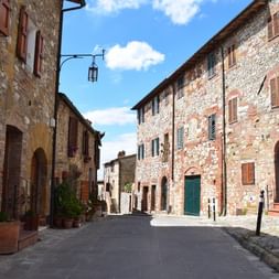 Rue pavée étroite à Cortona bordée de bâtiments médiévaux en pierre avec volets terracotta et portes voûtées sous ciel bleu.