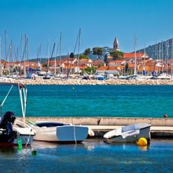 Marina à Biograd, Croatie avec petits bateaux au premier plan et mâts de voiliers. Bâtiments aux toits rouges et clocher visibles sur eau turquoise.