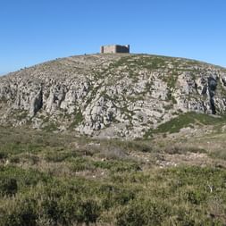 Château en pierre couronnant une colline calcaire rocheuse à Torroella de Montgrí, Costa Brava. La colline est couverte de maquis méditerranéen sous un ciel bleu.