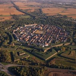Vue aérienne de la ville fortifiée Neuf-Brisach Vue aérienne de Neuf-Brisach montrant la ville fortifiée en étoile avec des bastions géométriques entourée de champs et forêts.