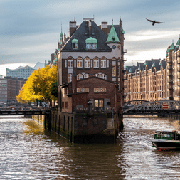 Vue du canal de Speicherstadt à Hambourg avec entrepôts en brique rouge, ponts et bateau. Oiseau volant au-dessus de l'eau sous ciel nuageux.