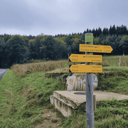 Panneaux directionnels jaunes sur le Chemin de Stevenson indiquant les distances vers Chasseradès et L'Estampe, avec banc en pierre et collines boisées.