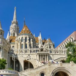 Bastion des pêcheurs à Budapest avec tours en pierre blanche, toit en tuiles colorées de l'église Matthias et grand escalier sous ciel bleu.