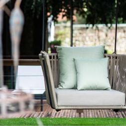 Fauteuil suspendu en bois avec coussins vert menthe dans le jardin de l'Hôtel Chambard, Kaysersberg, avec mur de pierre en arrière-plan.