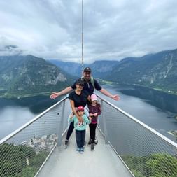 Famille de quatre personnes sur plateforme d'observation métallique surplombant le lac de Hallstatt et les montagnes du Salzkammergut autrichien.