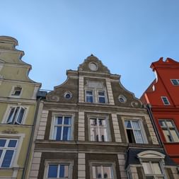 Rangée de façades colorées de bâtiments historiques à Stralsund avec pignons ornés. Bâtiments jaunes, gris et rouges avec cadres de fenêtres blancs sous ciel bleu.