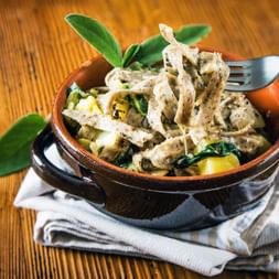 Bol de pâtes pizzoccheri avec nouilles de sarrasin, légumes et fromage, garni de feuilles de sauge, servi dans un plat en terre cuite.