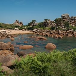 Baie côtière à Ploumanac'h avec rochers de granit rose, eau turquoise, plage de sable et végétation verte sous ciel bleu.