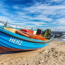 Bateau de pêche bleu immatriculé HER2 échoué sur la plage de sable d'Usedom. Le bateau contient des filets et équipements de pêche.