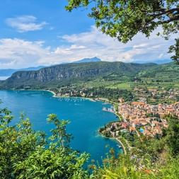 Vue panoramique du lac de Garde depuis Rocco del Garda montrant les eaux turquoise, la ville lacustre aux toits rouges et les montagnes.