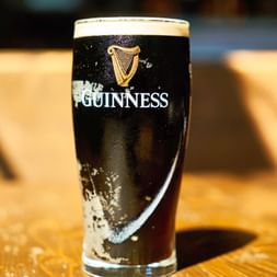 Un verre pinte plein de Guinness stout avec sa bière noire distinctive et sa mousse blanche crémeuse épaisse, avec le logo harpe iconique sur le verre.