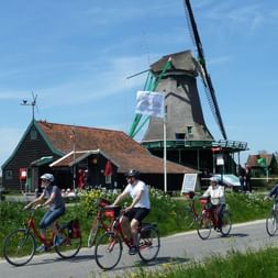 Groupe de cyclistes sur des vélos rouges pédalant devant un moulin hollandais traditionnel à toit vert en Hollande septentrionale.