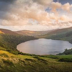 Vue panoramique d'un lac calme niché entre des collines verdoyantes sur le Wicklow Way, Irlande, sous un ciel nuageux dramatique.