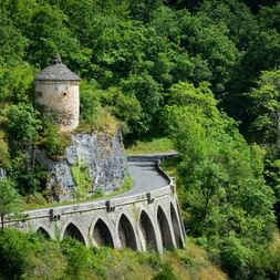 Viaduc historique en pierre à sept arches serpentant à travers la forêt verdoyante près de Rocamadour. Une tour ronde en pierre sur un rocher.