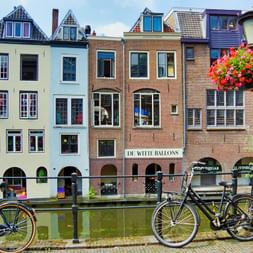 Vélos noirs garés le long d'un canal à Utrecht avec des maisons hollandaises colorées et des paniers de fleurs.