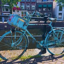 Vélo turquoise avec panier avant garé près d'un canal en Hollande. Maisons néerlandaises traditionnelles visibles de l'autre côté de l'eau.