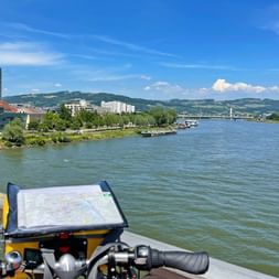 Guidon de vélo avec porte-carte surplombant le Danube à Linz. Église historique et bâtiments modernes visibles sur la rive.