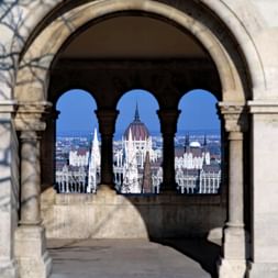 Vue à travers les arches en pierre du Bastion des Pêcheurs à Budapest, encadrant le Parlement hongrois avec son dôme distinctif.