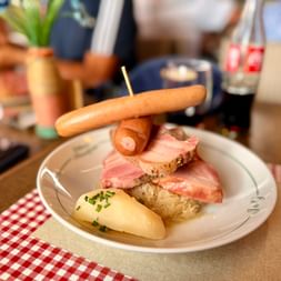 Assiette avec saucisse, tranches de jambon, pomme de terre et choucroute sur nappe à carreaux. Cadre de la route des vins d'Alsace.