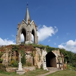 Clocher gothique de la chapelle Notre-Dame de la Motte près de Vesoul, sur des ruines en pierre avec entrée voûtée sous ciel bleu.