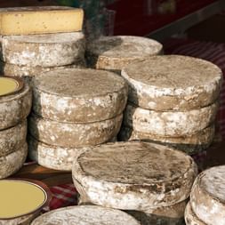 Plusieurs meules de fromage Tome des Bauges à croûte naturelle gris-blanc empilées sur un étal de marché, montrant l'aspect traditionnel affiné.