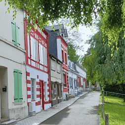 Rangée de maisons traditionnelles avec volets verts et rouges le long d'une rue pavée près de la Côte d'Opale et Baie de Somme, avec saules.