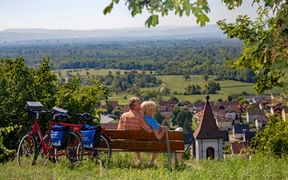Couple de cyclotouristes profitent d'une pause détente sur un banc surplombant un vignoble de la Forêt-Noire du Sud