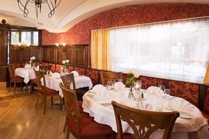 Intérieur de restaurant élégant avec nappes blanches, chaises en bois, papier peint rouge à motifs et plafond voûté avec lustre.