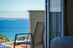 Vue depuis le balcon de l'Hôtel Palazzo del Garda montrant les eaux bleues du lac de Garde, le rivage lointain et une chaise de balcon.