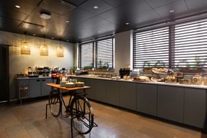 Espace buffet petit-déjeuner moderne à l'Elite Hotel Arcadia Stockholm avec armoires grises, suspensions et table vélo décorative.