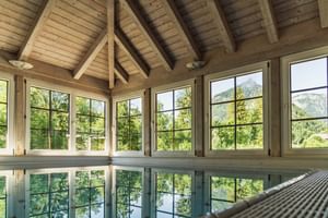 Piscine intérieure du Bergrose Hideaway avec plafond à poutres apparentes et grandes fenêtres donnant sur les montagnes vertes et forêts.