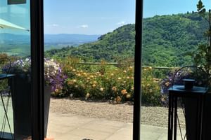 Vue depuis la terrasse du Le Valli Agriturismo montrant un jardin fleuri avec des fleurs violettes et jaunes, collines vertes en arrière-plan.