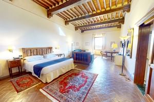 Chambre supérieure spacieuse avec poutres apparentes, sol en terre cuite, lit en bois, jacuzzi bleu, tapis persans et coin salon.