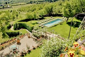 Vue aérienne du jardin de l'Hôtel Palazzo Squarcialupi avec piscine rectangulaire, transats, pelouses soignées, parterres de fleurs et paysage viticole.