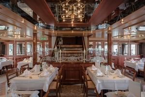 Intérieur élégant du restaurant du MS Switzerland avec tables nappes blanches, chaises en bois et roue à aubes sous plafond miroir.
