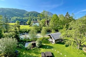 Vue sur jardin verdoyant de l'Hotel Bergrose avec pavillon en bois, pelouse et montagnes boisées en arrière-plan sous ciel bleu.
