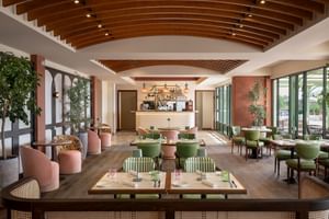 Intérieur élégant du restaurant Villa Ermellina avec poutres de plafond en bois courbées, chaises rembourrées roses et vertes, tables dressées.