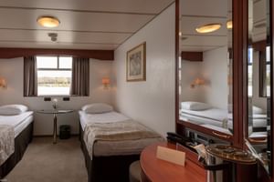 Cabine double sur le pont principal du MS Switzerland avec deux lits, vue par fenêtre, meubles en bois, miroir, appliques murales et décor beige-brun.