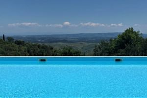 Piscine bleue au Le Valli agriturismo avec vue panoramique sur les collines toscanes, champs verts et montagnes lointaines sous ciel bleu.