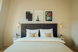Chambre d'hôtel moderne avec tête de lit géométrique sombre, literie blanche, coussins décoratifs, trois œuvres encadrées au-dessus du lit.