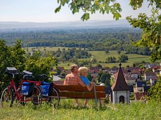 Couple de cyclotouristes profitent d'une pause détente sur un banc surplombant un vignoble de la Forêt-Noire du Sud
