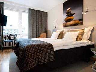 Chambre double moderne à l'Hôtel Birger Jarl Stockholm avec literie blanche, plaid à motifs, œuvre zen et vue sur la ville.